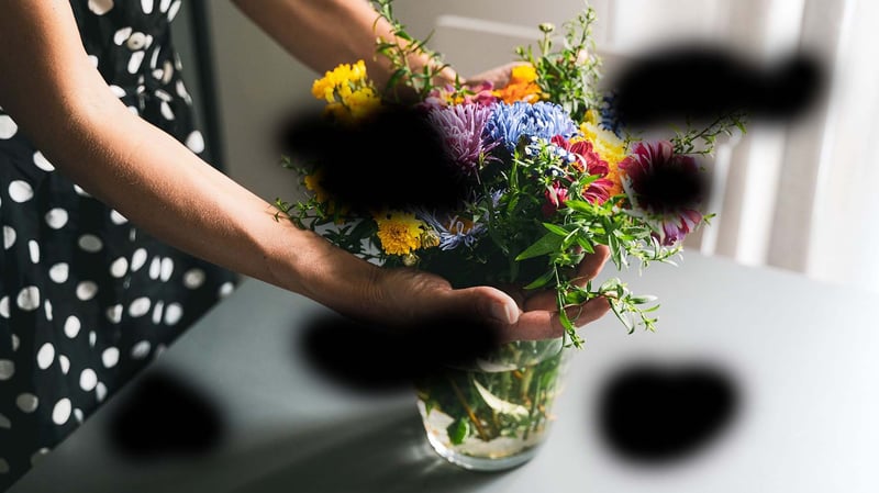 Image shows hands holding a vase of flowers in a well lit room. Large, blurred black splodges appear at random, obscuring some parts of the image, which is what someone with diabetic retinopathy might experience.