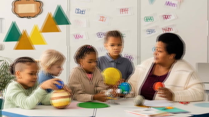 Image shows young children and a teacher in a classroom. Each item in the class appears as a double, overlapping image, which gives a blurred impression.